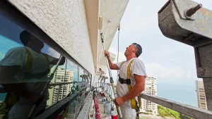 Two contractors on scaffolding repaint the exterior walls of a residential complex