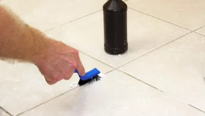 Contractor scrubbing grout lines with a coarse brush