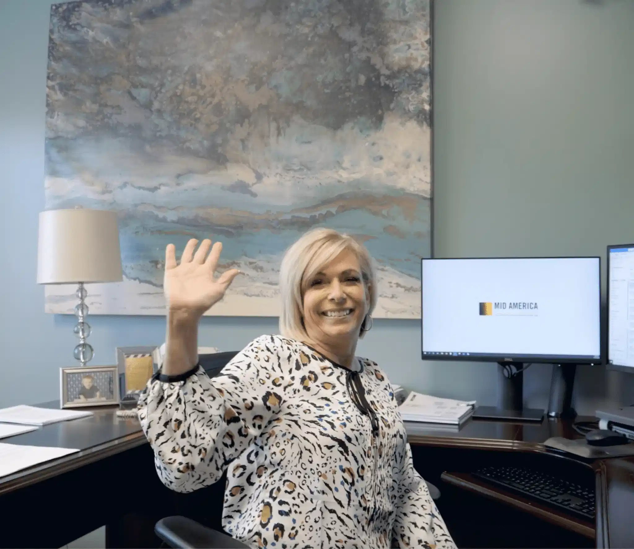 Female employee smiling and waving at camera from her desk